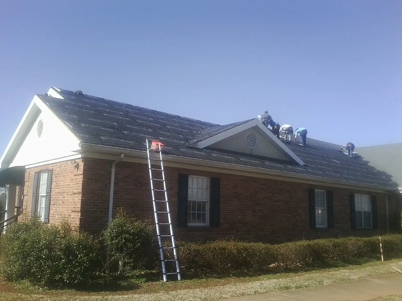 Crew tearing shingles off a brick ranch roof with a ladder set — Emergency Roof Repair work by our crew in Barkhamsted