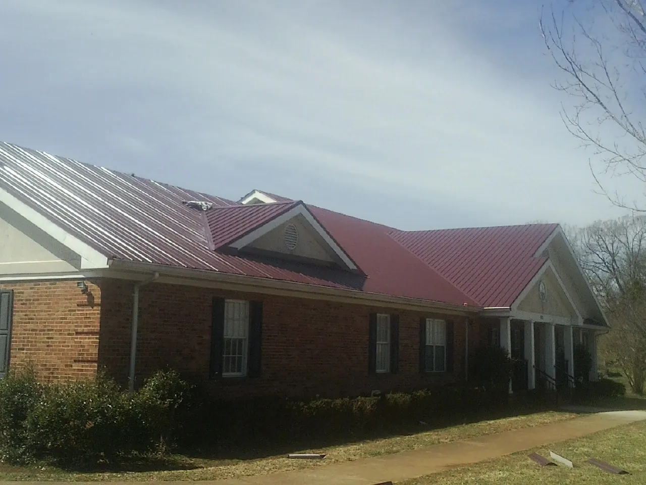 Red metal roof with gabled entries on a long brick building, from a Hail Damage Roof Repair job in Barkhamsted