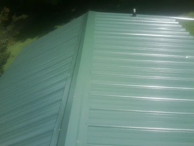 New green metal panels meeting at the ridge of a roof — Flat Roof Repair work by our crew in Barkhamsted