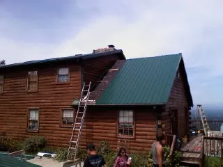 Green metal roof going on a two story log home with ladders set in Barkhamsted