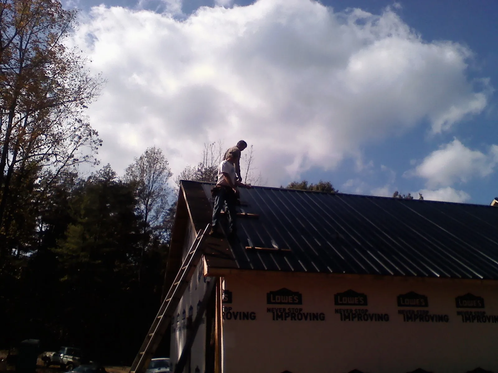 Roofer fastening dark metal panels high against a cloudy sky, from a Roof Inspection job in Barkhamsted
